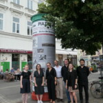 grupa ludzi pozuje na tle słupa ogłoszeniowego